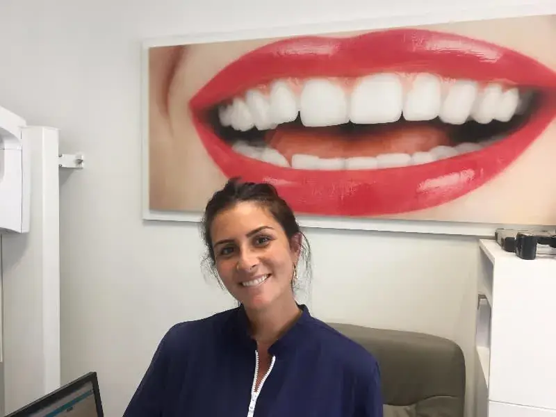 Dr Laura Zeitoun Saal in front of a large framed photograph of a smile, in a treatment room at the practice